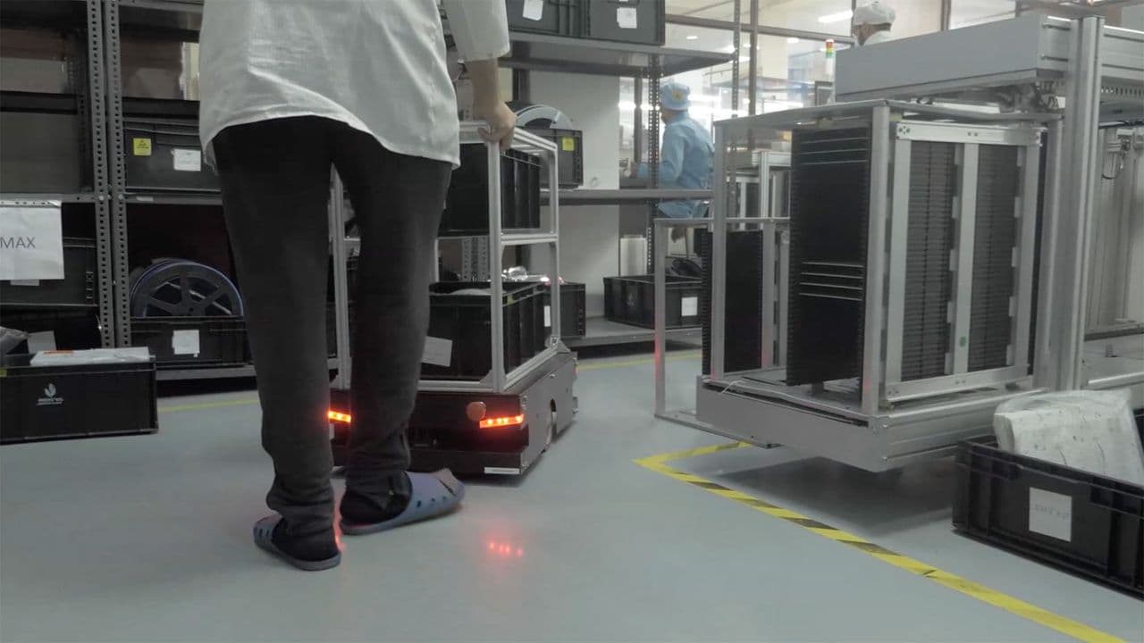 Peer Robotics autonomous mobile robot moving a cart past a worker in a warehouse aisle