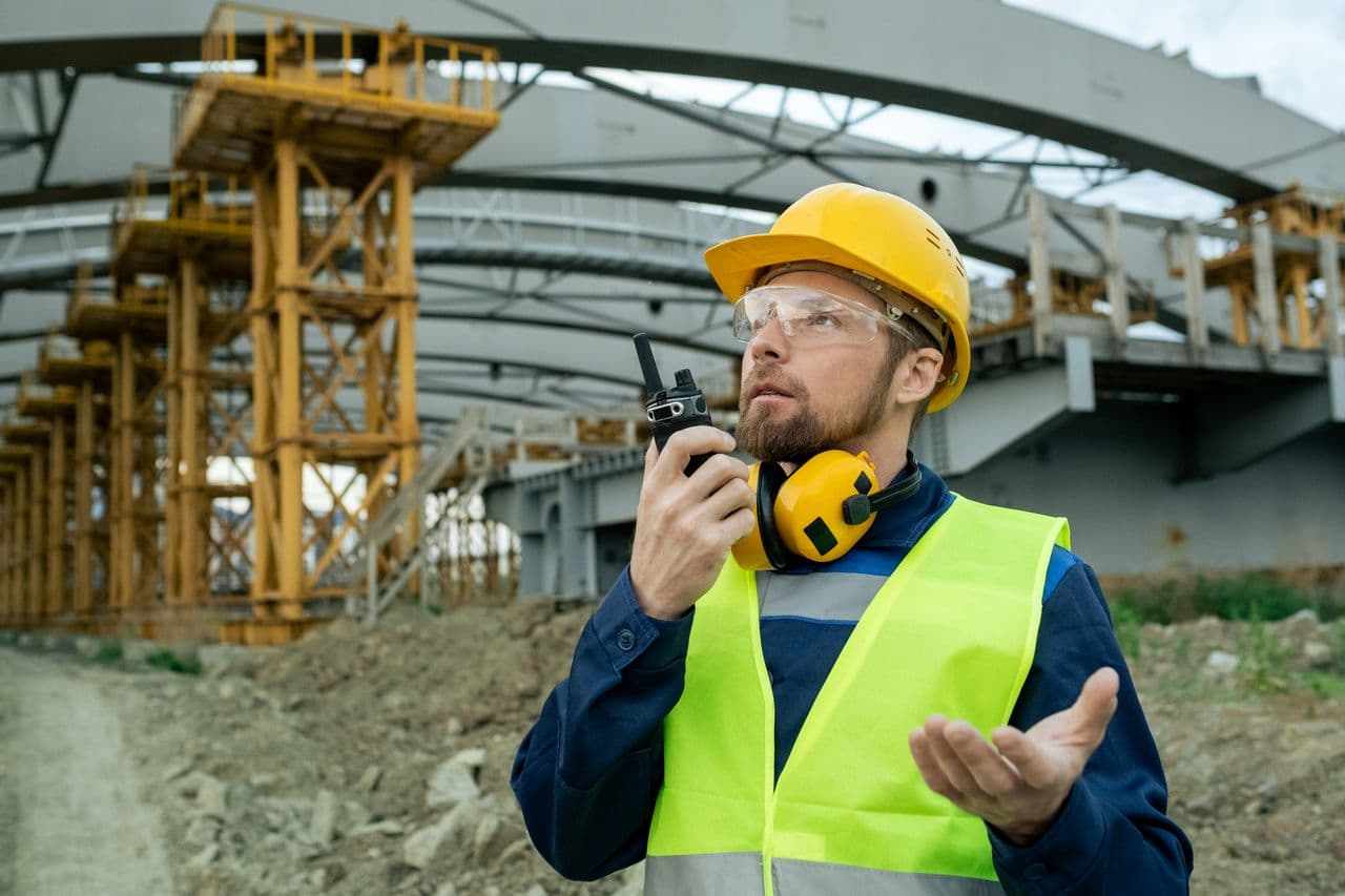 Supervisor in hard hat and ear defenders talking on a radio